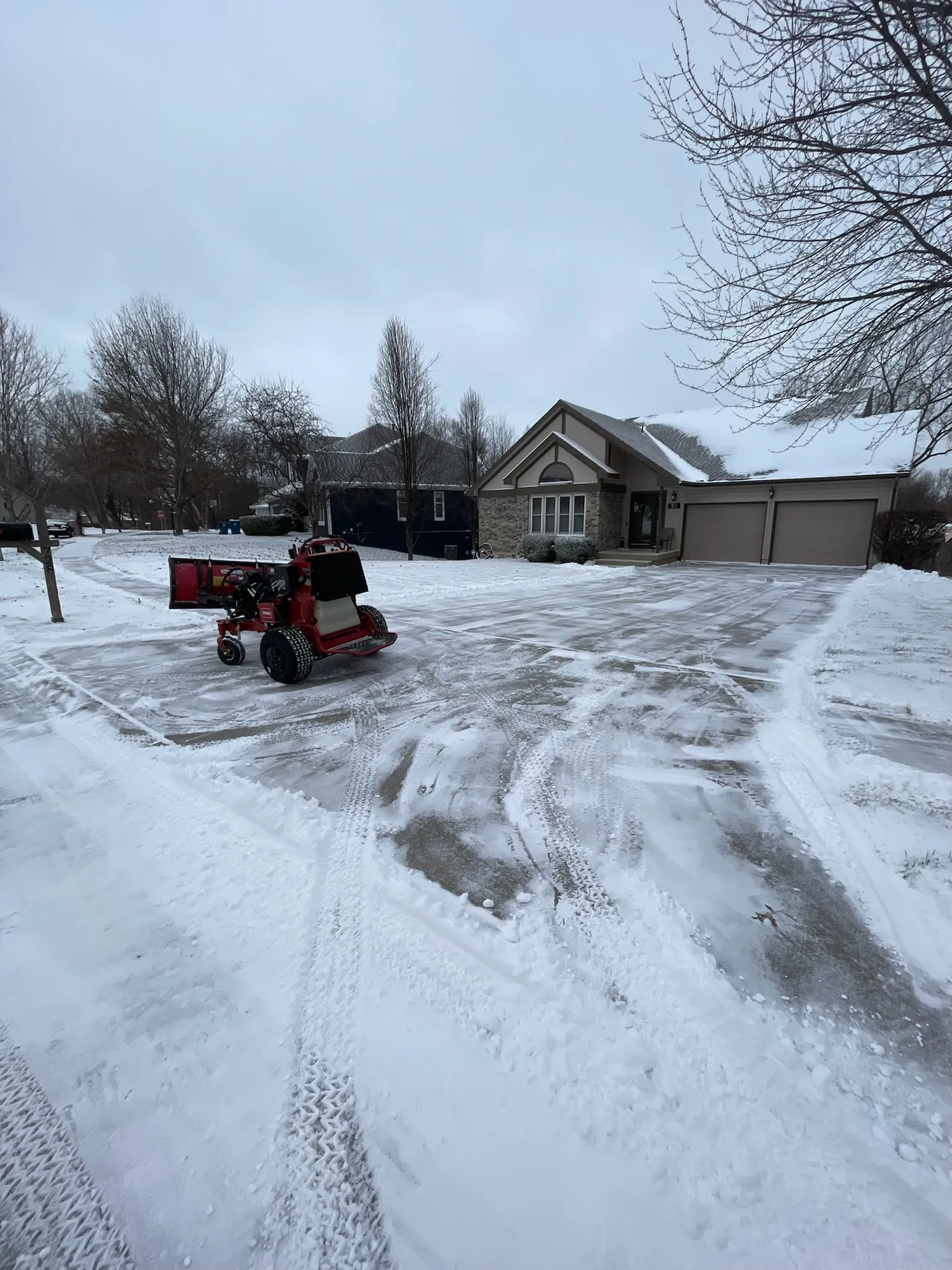Stand-on plow parked on a cleared residential driveway after an overnight snow