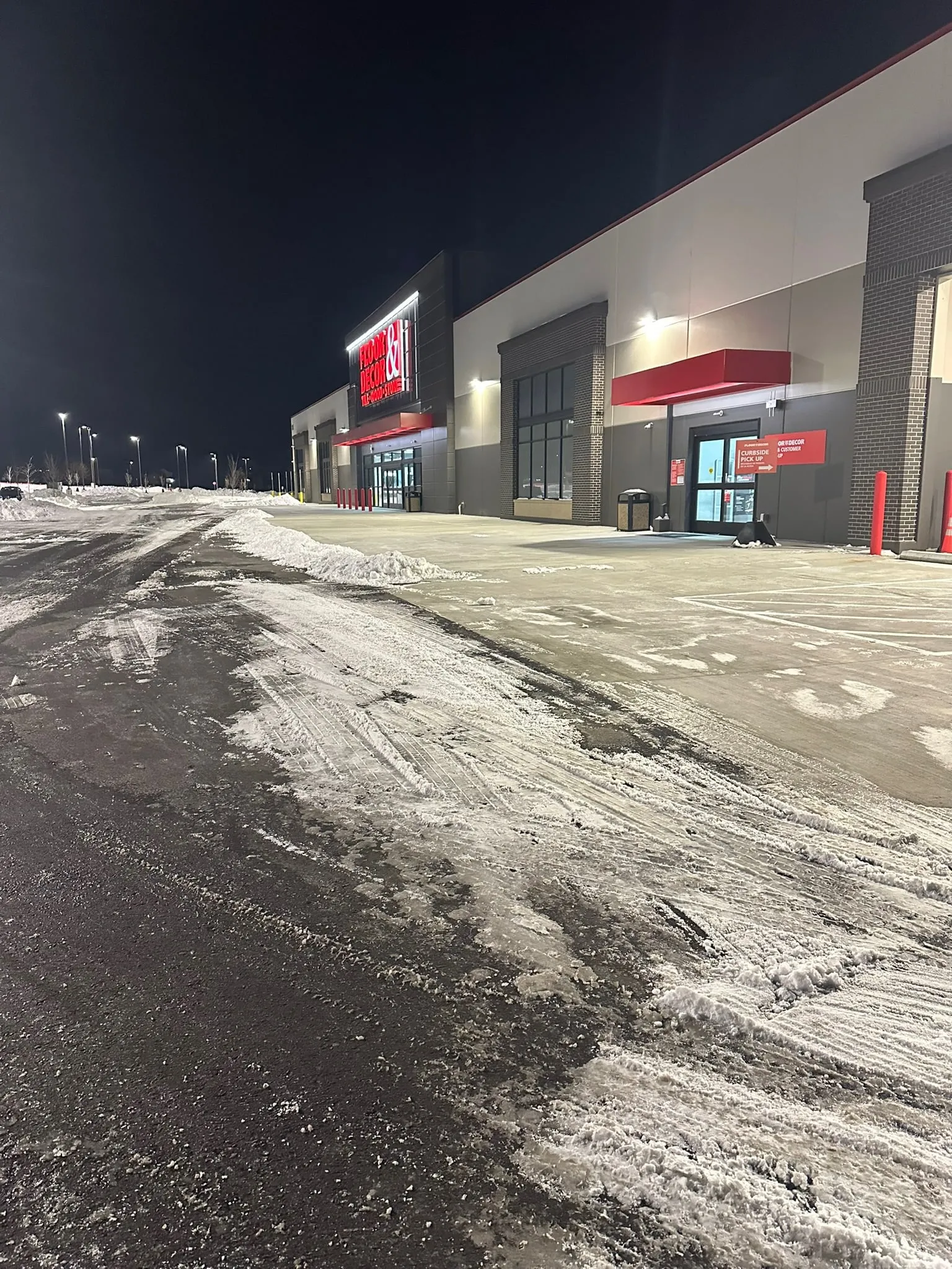 Cleared storefront walkway at night contrasted against the untouched snowy lot