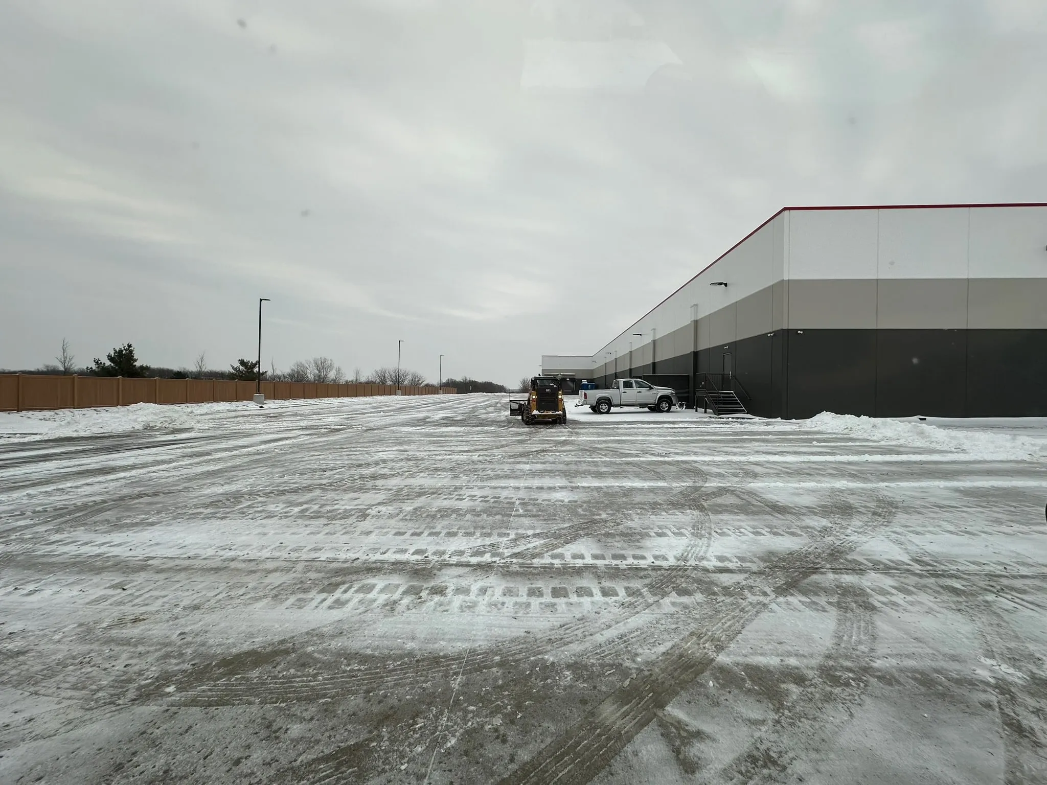 Skid steer with plow attachment parked at a commercial loading area next to the service truck